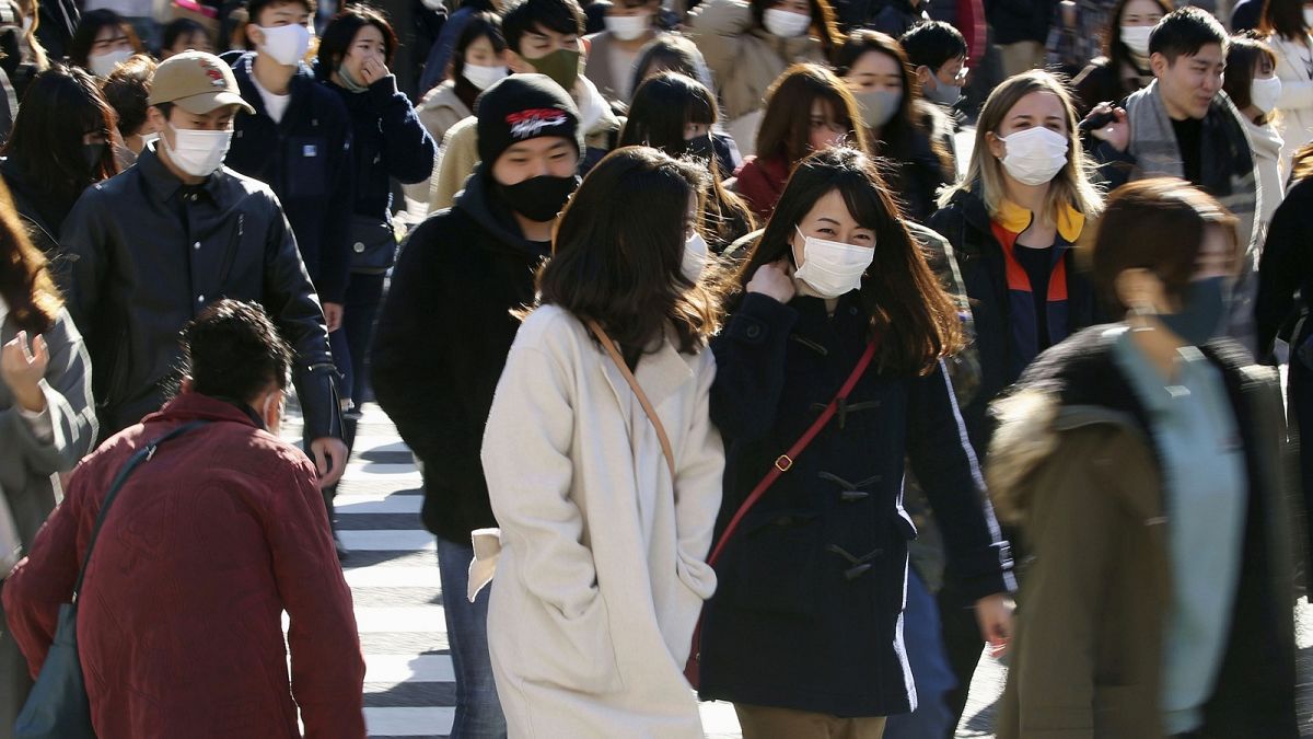 People wearing face masks to help curb the spread of the coronavirus walk around the scrambled intersection at the Shibuya shopping district in Tokyo Saturday, Dec. 26, 2020.