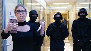 Ljubov Szobol a korrupcióellenes alapítvány irodai folyosóján, mögötte rendőrökkel, 2019-ben
