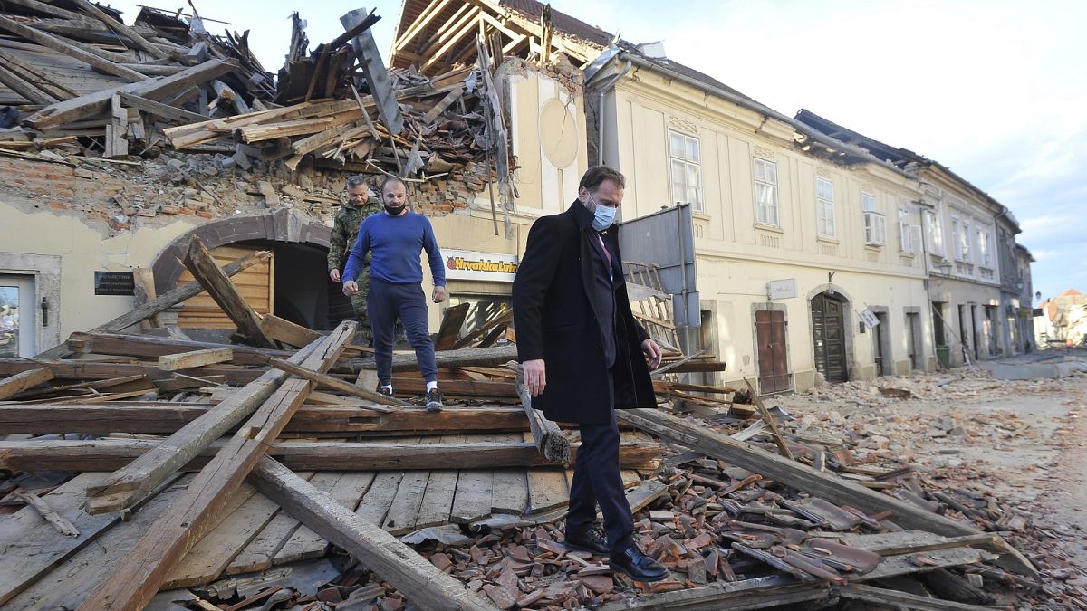 People move through remains of a building damaged in an earthquake, in Petrinja, Croatia, Tuesday, Dec. 29, 2020. 