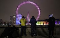 A small group of people look across from the embankment towards the London Eye ferris wheel by the River Thames in London as the New Year starts in London, Friday, Jan 1, 2021