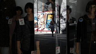 Α woman wearing a face mask against the spread of coronavirus, is reflected on the mirror of a closed shop in Athens
