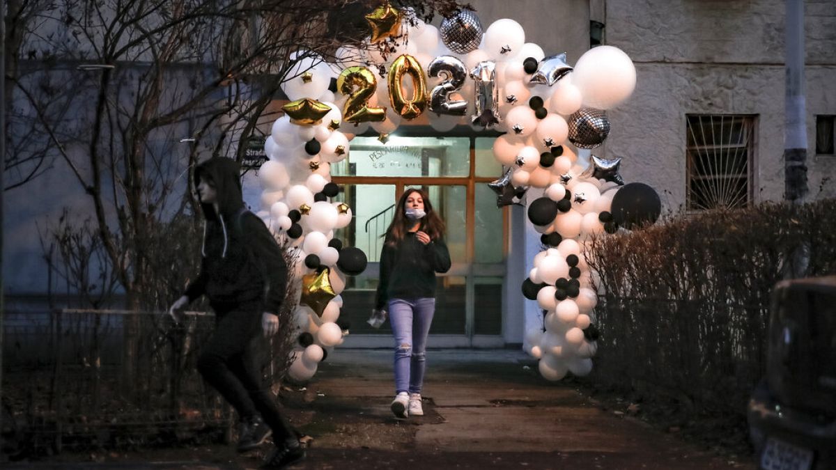 Children stand in the doorway of an apartment building, framed by a a new year's balloon decoration in Bucharest, Romania, Friday, Jan. 1, 2021. 