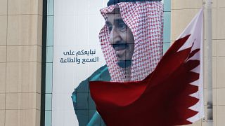 علم قطري يرفرف أمام لافتة تظهر الملك السعودي سلمان في مركز تجاري في الرياض، المملكة العربية السعودية.