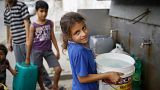 Thirteen-year-old Israa holds a bucket filled with potable water from a public water point in Khan Younis, Gaza Strip.