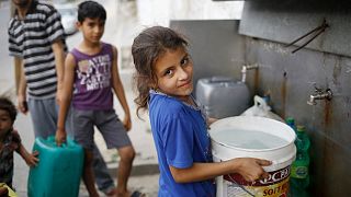 Thirteen-year-old Israa holds a bucket filled with potable water from a public water point in Khan Younis, Gaza Strip.