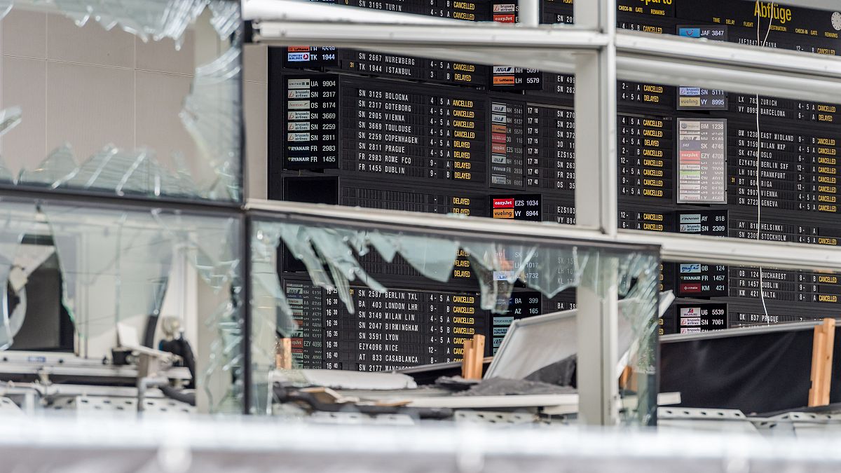 In this March 23, 2016 file photo, an arrivals and departure board is seen behind blown out windows at Zaventem Airport in Brussels.