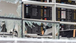 In this March 23, 2016 file photo, an arrivals and departure board is seen behind blown out windows at Zaventem Airport in Brussels.