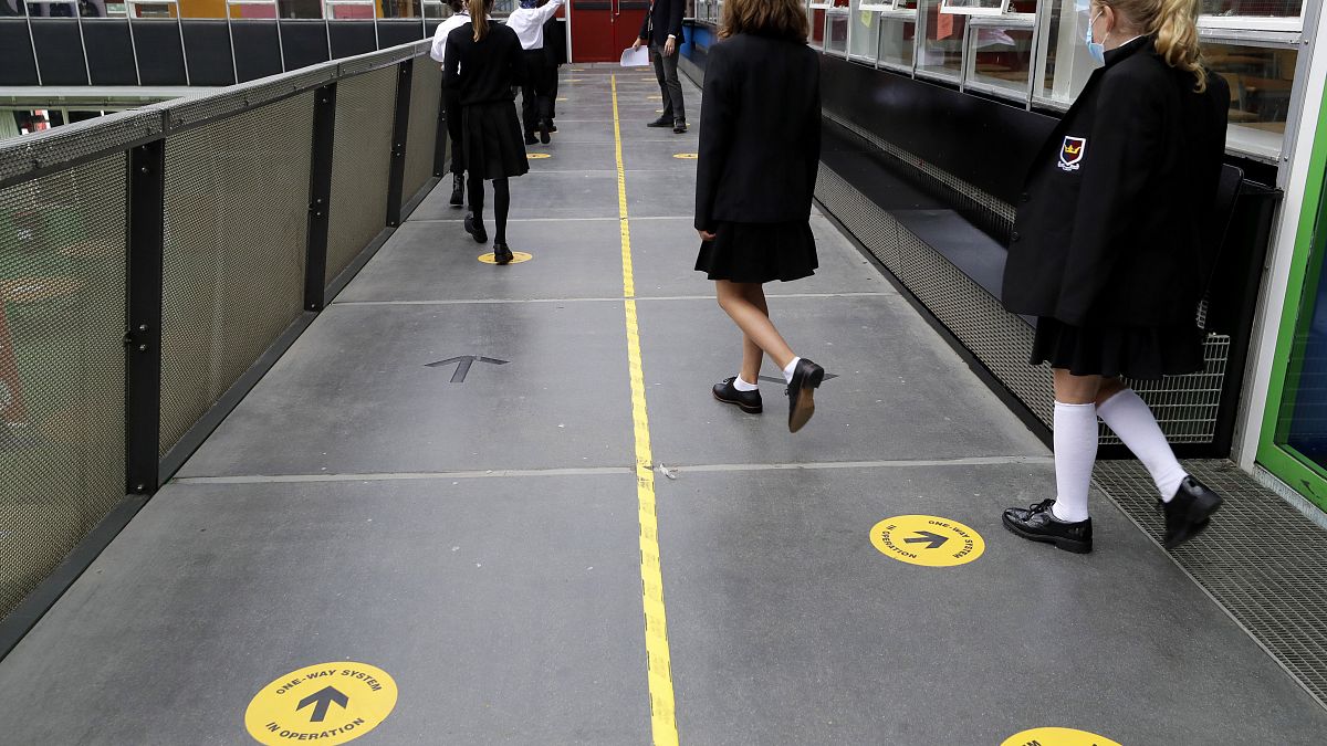 Pupils follow social distancing signs as they walk along a school corridor