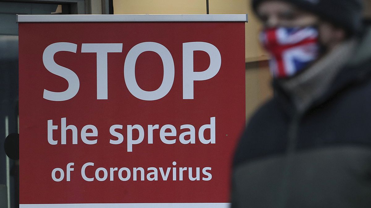 Un hombre con mascarilla pasa ante un cartel "Detener la propagación de coronavirus" en Glasgow