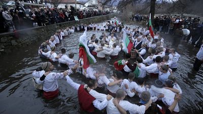 Dozens of citizens of the mountain town of Kalofer, in central Bulgaria, clad in traditional dresses stand in the icy Tundzha River
