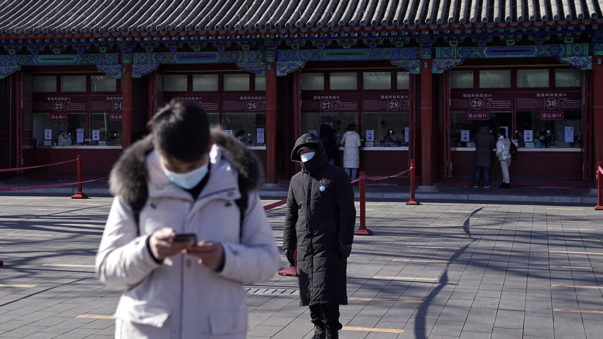 A man wearing a face mask to help curb the spread of the coronavirus browses his smartphone as a masked security guard stands near the quiet ticket counters in Beijing. 