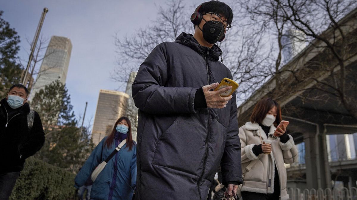 A man wearing a face mask and a disposable gloves to help curb the spread of the coronavirus heads to work with other masked people during the morning rush hour in Beijing.