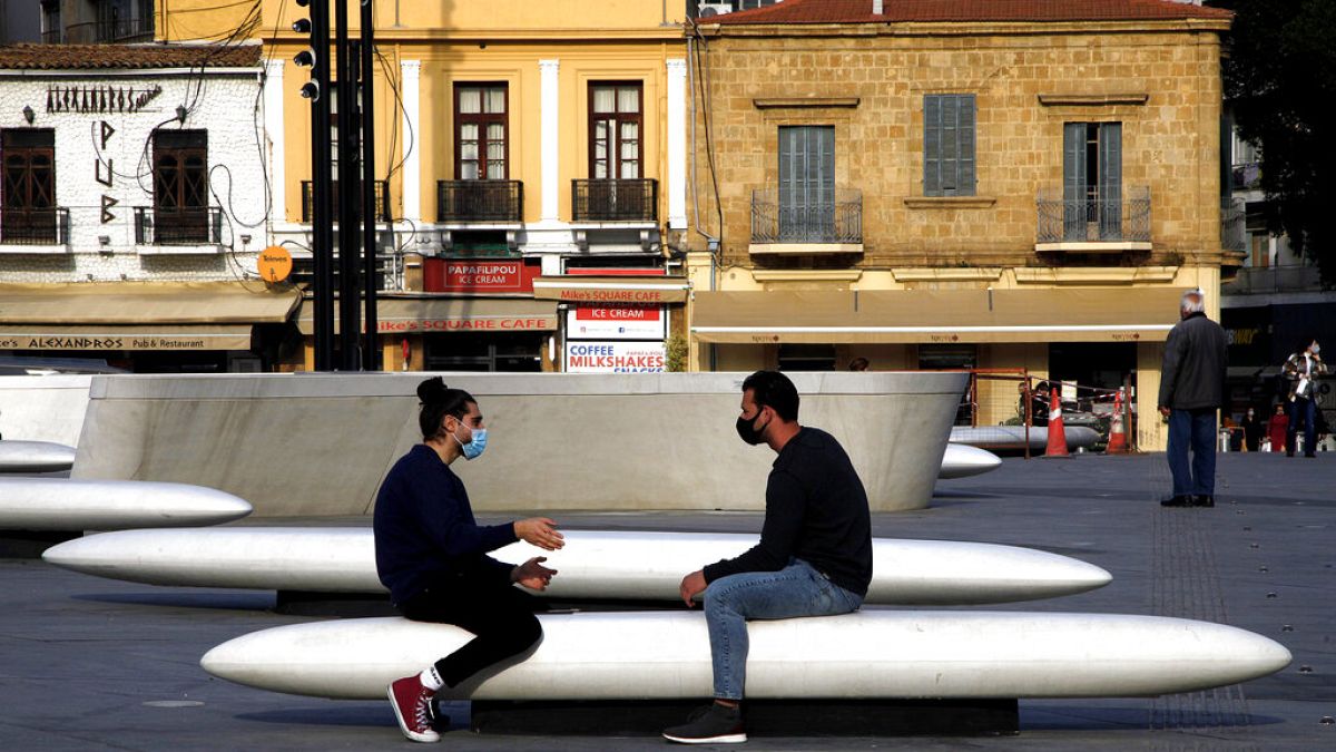 Men wearing face masks to prevent the spread of coronavirus talk on a bench at Elefphtheria, Liberty, square in central Nicosia
