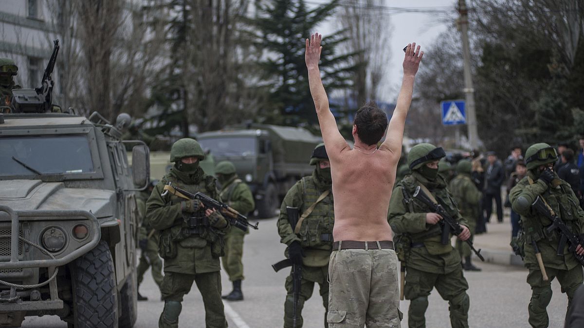 رجل أوكراني يقف متظاهرًا أمام مسلحين يرتدون زيًا عسكريا في ضواحي سيفاستوبول، إحدى مدن شبه جزيرة القرم/ 1 مارس 2014 
