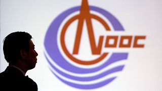 FILE - A man stands in front of the screen featuring logo of CNOOC Limited in Hong Kong, March 29, 2005