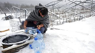 Un migrant utilise des bouteilles en plastique pour récupérer de l'eau, le 11 janvier 2021, dans le camp de Lipa, Bosnie