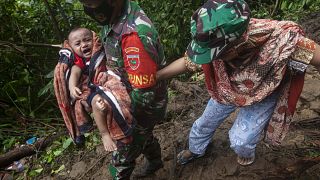 Un soldat aide une femme en portant son bébé dans une zone touchée par un glissement de terrain après le séisme, près de Mamuju, Indonésie, le 16 janvier 2021