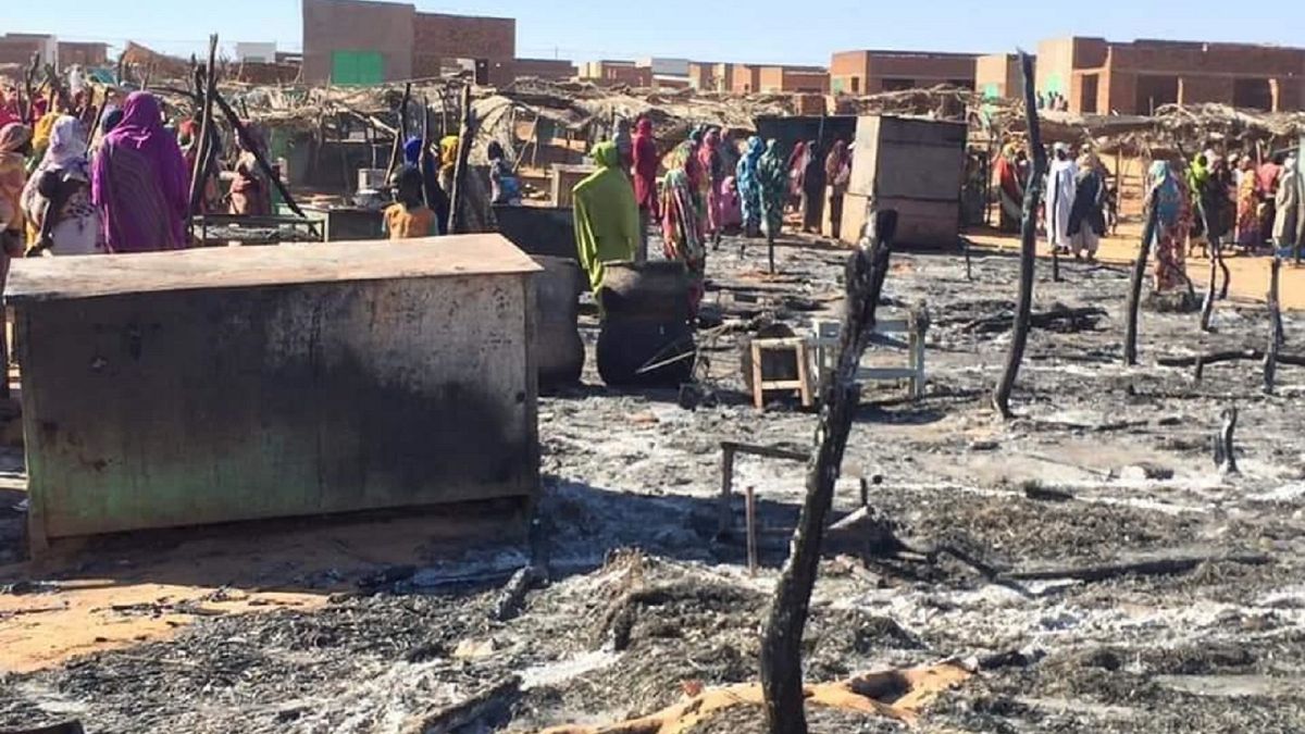 In this Dec. 29, 2019 file photo, residents of a refugee camp gather around the burned remains of makeshift structures, in Genena, Sudan.