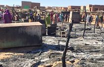 In this Dec. 29, 2019 file photo, residents of a refugee camp gather around the burned remains of makeshift structures, in Genena, Sudan.