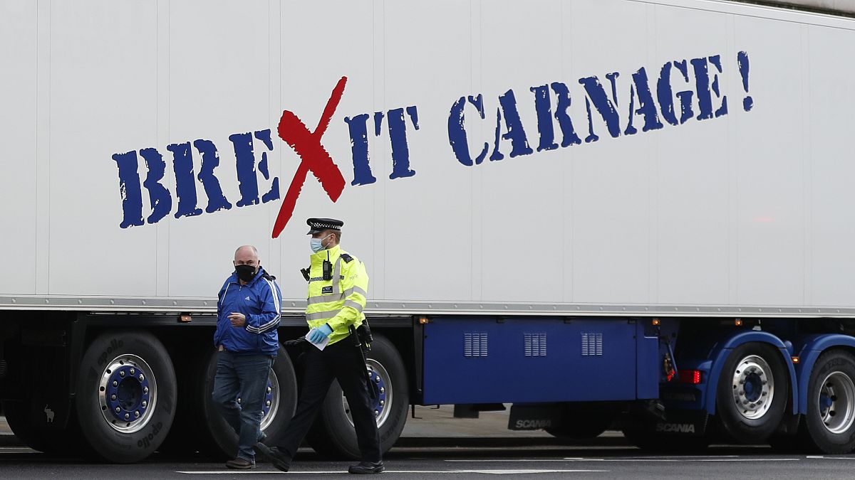 A policeman escorts the driver of a shellfish export truck as he is stopped for an unnecessary journey in London, Monday, Jan. 18, 2021, during a protest by exporters.