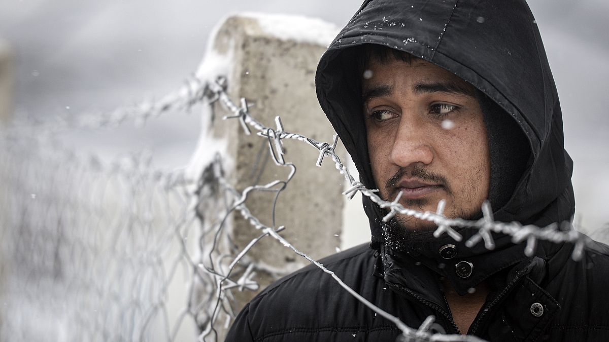 A migrant stands next to a fence during snowfall at the Lipa camp, outside Bihac, Bosnia, Friday, Jan. 8, 2021.