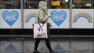 A woman with face covering walks past windows of the London Bridge tube station with signs to support the NHS in London, Thursday, Jan. 14, 2021.