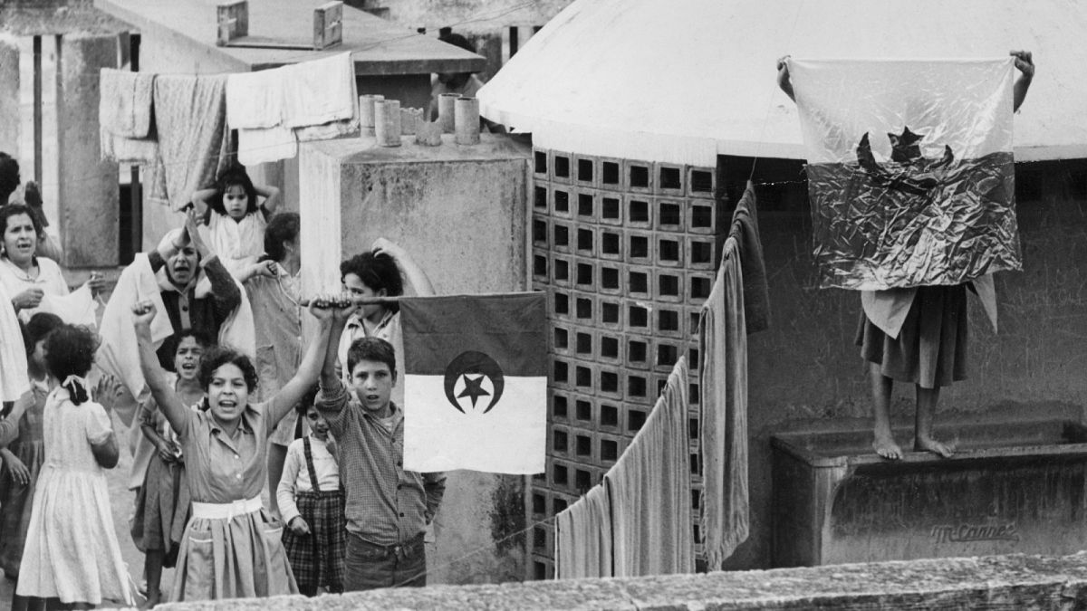 1  نوفمبر 1961، على سطح أحد المنازل في الجزائر العاصمة، شبان يلوحون بأعلام الجزائر احتفالاً بعيد الاستقلال الجزائري.