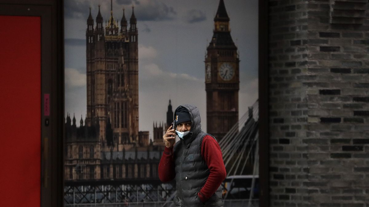 A man wears a mask as he passes a poster showing Big Ben in London, Wednesday, Jan. 20, 2021.