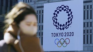 A woman wearing a protective mask to help curb the spread of the coronavirus walks near a banner of the Tokyo 2020 Olympics in Tokyo Tuesday, Jan. 19, 2021.