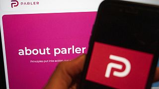 The logo of the social media platform Parler is displayed in Berlin, Jan. 10, 2021. In the background on a screen is the platform's website.
