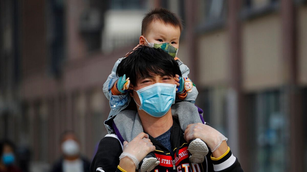 A man carries a toddler on his shoulders as both wear protective face masks to help prevent the coronavirus outbreak walk on a street in Beijing