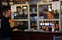 A man orders beer behind a safety screen at the Forester pub in London, Saturday, July 4, 2020