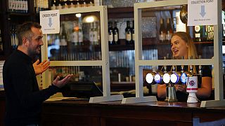 A man orders beer behind a safety screen at the Forester pub in London, Saturday, July 4, 2020