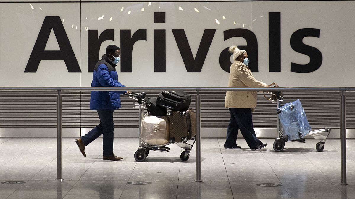 Arriving passengers walk past a sign in the arrivals area at Heathrow Airport in London, Tuesday, Jan. 26, 2021