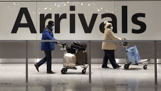 Arriving passengers walk past a sign in the arrivals area at Heathrow Airport in London, Tuesday, Jan. 26, 2021