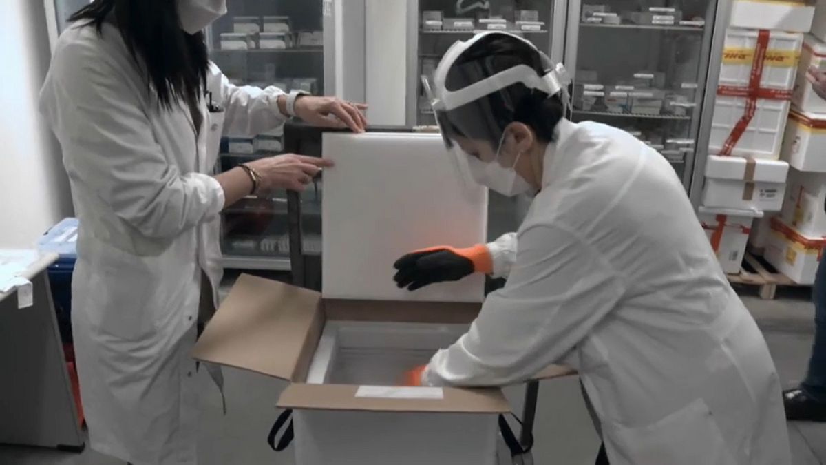 Healthcare professionals counting and transferring vaccine vials from freezer to fridge in a hospital pharmacy in Livorno, Italy.