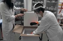 Healthcare professionals counting and transferring vaccine vials from freezer to fridge in a hospital pharmacy in Livorno, Italy.