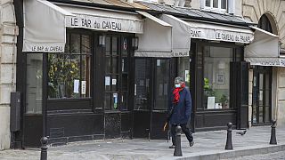 Una mujer camina frente a un restaurante cerrado en París.