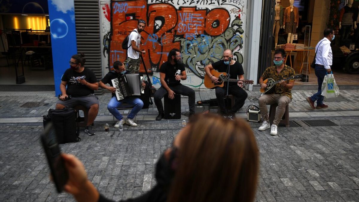 Musicians wearing face masks to prevent the spread of the coronavirus, perform as a woman records a video with her cellphone on Ermou Street, 