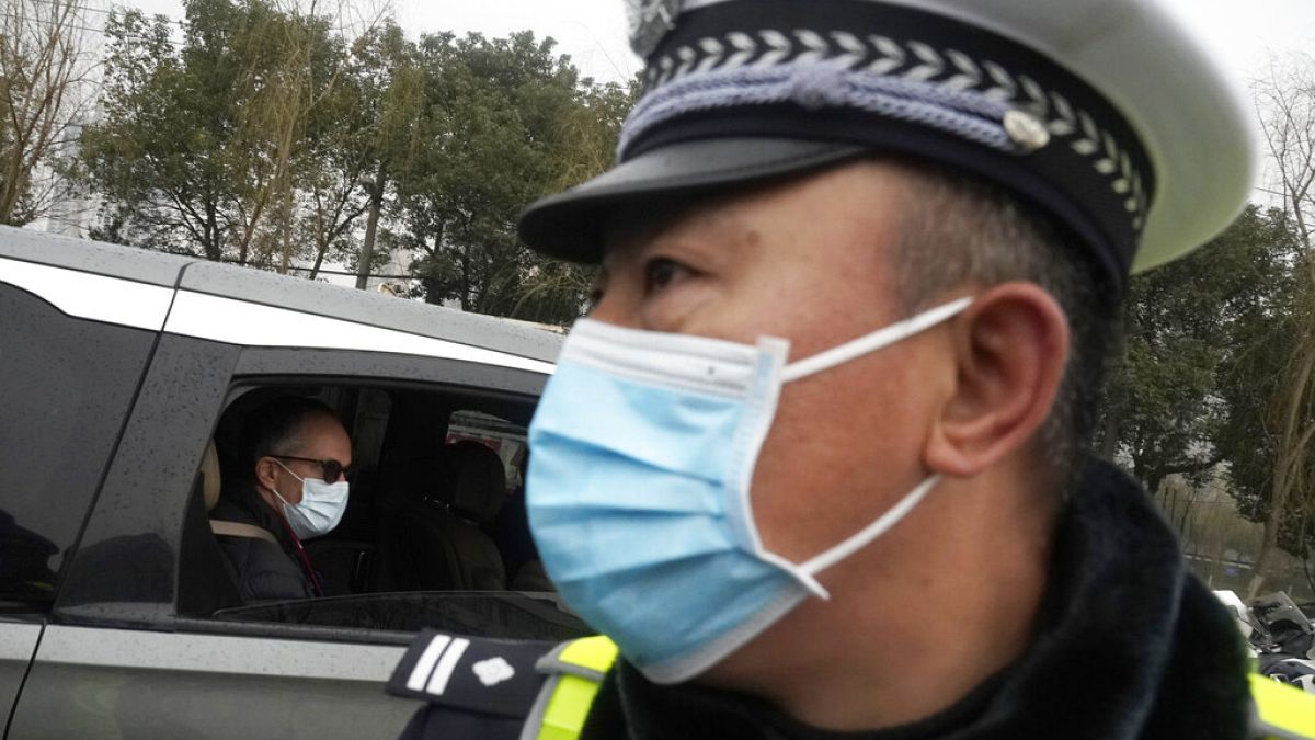 Peter Ben Embarek of the World Health Organization team passes by a Chinese police officer as he leaves in a convoy from the Baishazhou wholesale market
