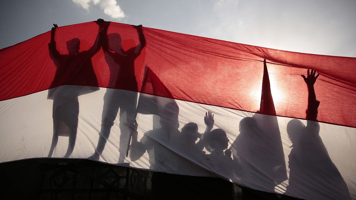 ظل يمنيين من وراء علم كبير لليمن أثناء حضورهم احتفالًا لإحياء ذكرى ثورة 1962 في صنعاء، اليمن.