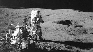 Apollo 14 astronaut Alan B. Shepard Jr. conducts an experiment near a lunar crater, using an instrument from a two-wheeled cart carrying various tools. 