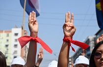 Manifestantes usam fitas vermelhas, cor do partido de Aung San Suu Kyi e fazem a saudação da resistência