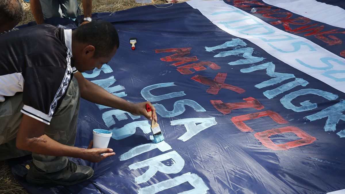 A Central American migrant paints a banner with messages in support of a migrant caravan trying to reach the US at Tecun Uman, Guatemala on the Mexican border, Jan. 22, 2020.