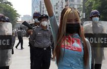 Protester posing for a photo in front of riot police line while holding a three-finger salute.