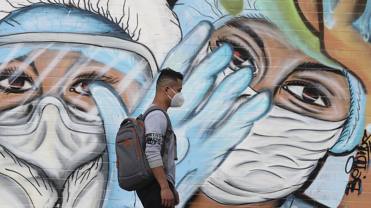 Un peatón pasa junto a un mural que promueve el uso de mascarillas protectoras para ayudar a frenar la propagación del COVID-19 en Quito, Ecuador.