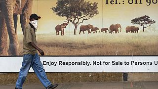 A man wearing a face covering, walks past a logo on the street in Alberton, near Johannesburg, South Africa, Thursday, Jan. 7, 2021.