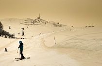 Skiers wearing protective face mask ski as Sahara sand colours the snow and the sky in orange in Anzere, Switzerland, on February 6 2021.
