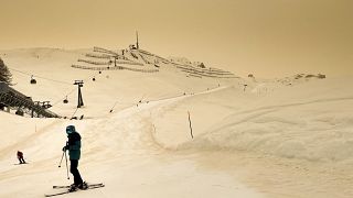 Skiers wearing protective face mask ski as Sahara sand colours the snow and the sky in orange in Anzere, Switzerland, on February 6 2021.