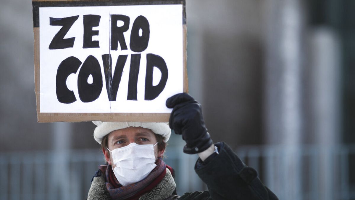 A demonstrator holds up a poster that reads: 'Zero COVID' in front of the chancellery in Berlin, Wednesday, Germany, Feb. 10, 2021, as he attends a protest.